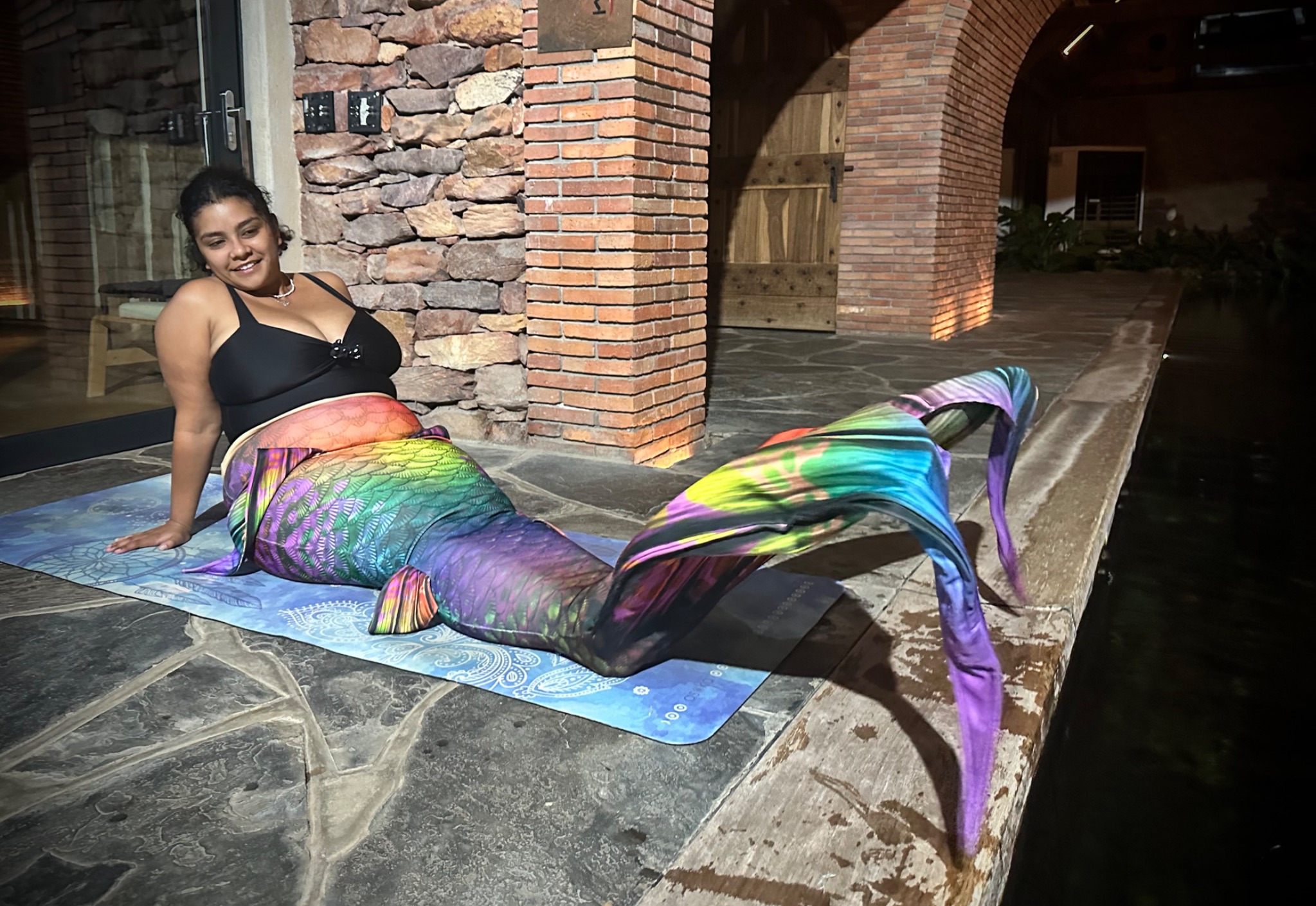 Smiling mermaid with a rainbow tail beside a swimming pool