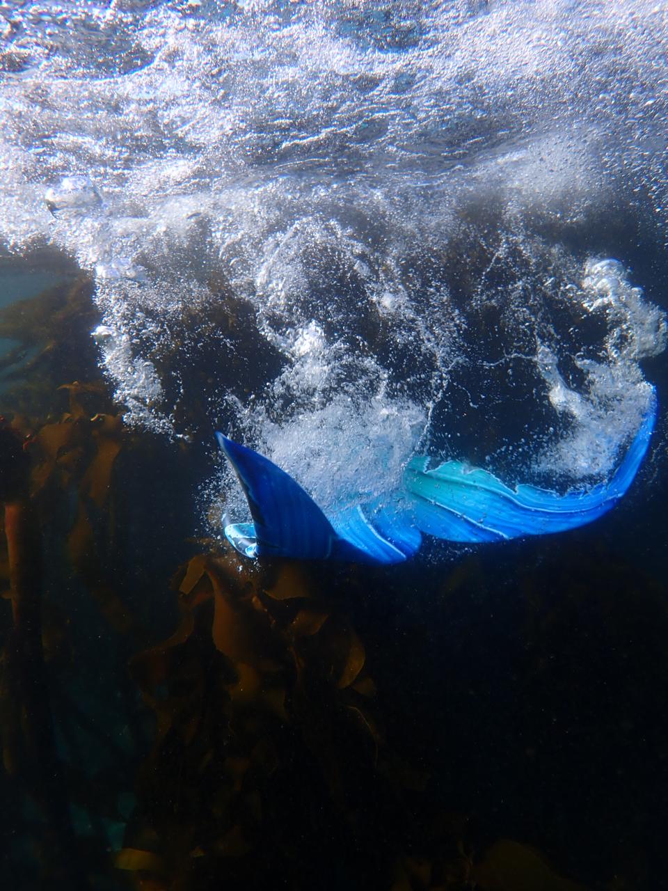 Blue mermaid tail moving through bubbles underwater