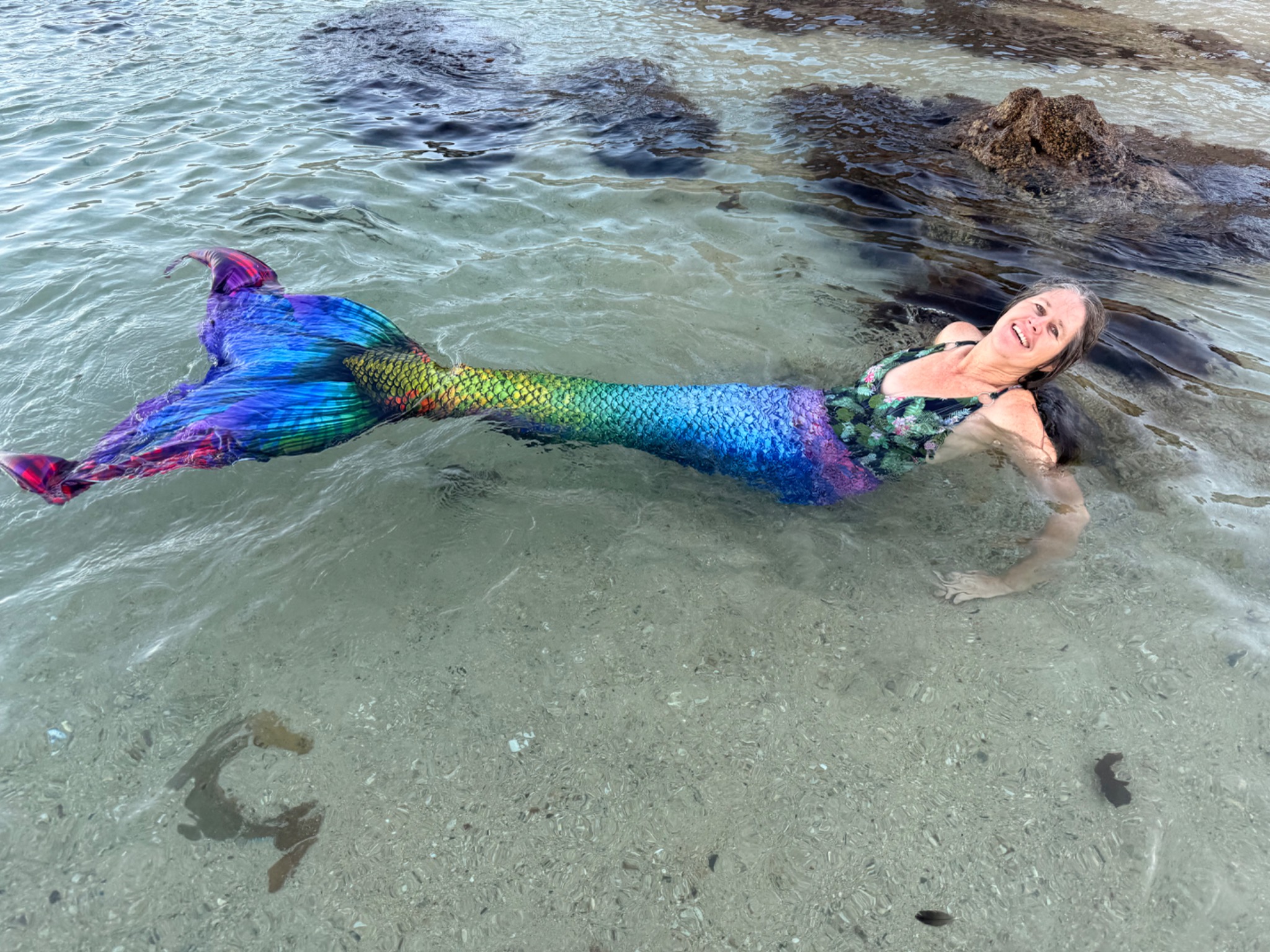 Rainbow-tailed mermaid floating in clear tidal water